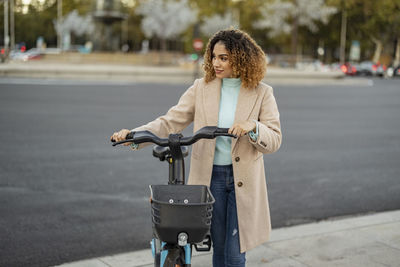 Woman with electric bicycle wheeling on footpath