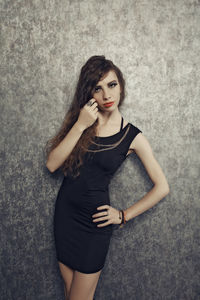 Portrait of young woman standing against wall
