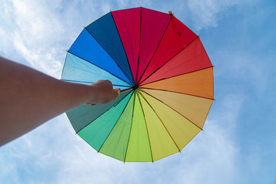 Human hand holding multicolored umbrella against sky