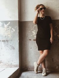 Young woman looking away while standing against wall