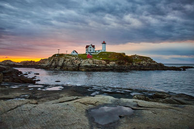 Lighthouse by sea against sky during sunset