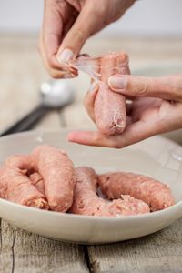 Cropped image of hand holding peeling sausage in bowl