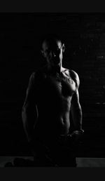 Portrait of shirtless man standing against black background