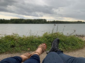 Low section of man by lake against sky