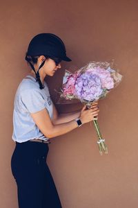 Side view of jockey holding fresh hydrangeas bouquets against wall