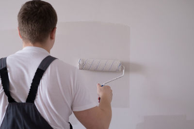 Painter man painting the wall white with a roller