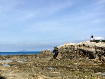 Man standing on rock by sea against sky