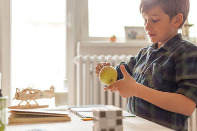 Cute elementary student playing with an apple while studying at home.