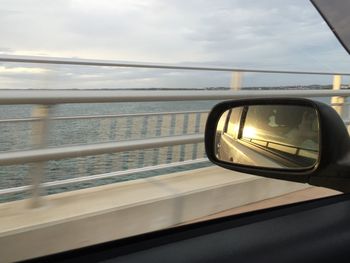 Side-view mirror on car by sea during sunset