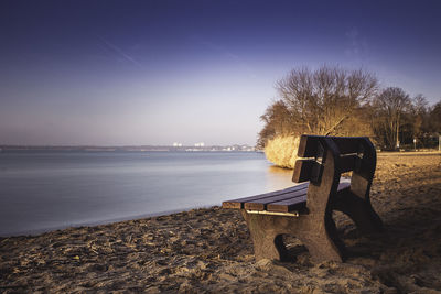 Empty bench on field by trees against sky