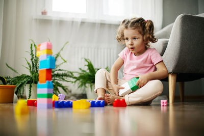 A little girl is sitting on the floor in the playroom and playing with colorful cubes
