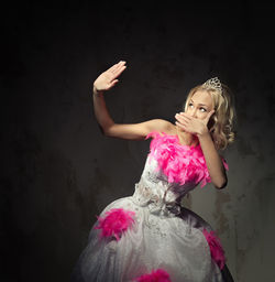 Beautiful young woman wearing pink and white wedding dress while gesturing stop sign against wall