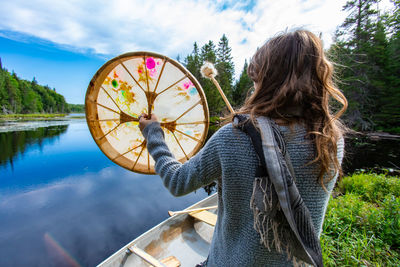 Rear view of woman holding umbrella by lake against sky