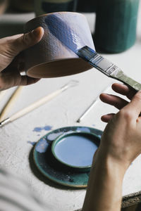 Female owner painting cup with brush in ceramics store