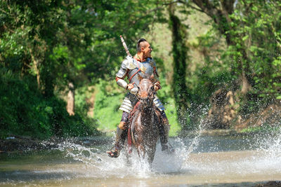 Man wearing warrior costume riding horse at forest