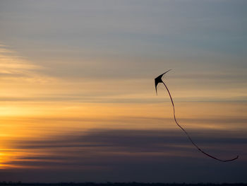 Low angle view of silhouette kite flying in cloudy sky during sunset
