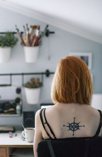 Rear view of woman with compass tattoo on back at home office