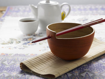 Close-up of bowl and chopsticks with teapot on table