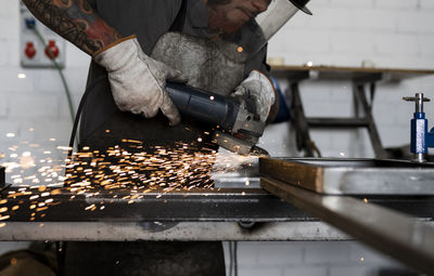 Side view of serious male welder using electric grinder and cutting metal detail in grungy workshop