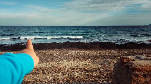 Cropped image of child pointing at waves in sea at beach