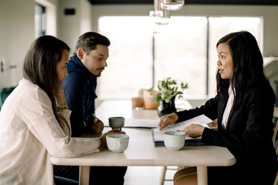 Customers discussing property documents with saleswoman at table in new house