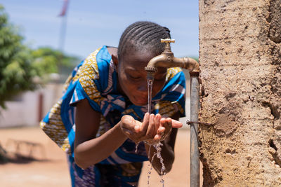 Girl drinking water from faucet against wall