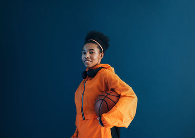 Portrait of young woman standing against blue background