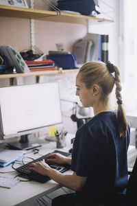 Female nurse with ponytail working on computer while sitting at desk in clinic