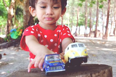 Boy playing with toy cars while standing by tree stump at park