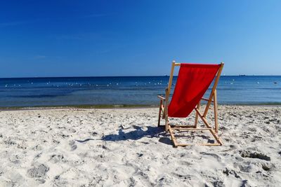 Deck chairs on beach against clear blue sky