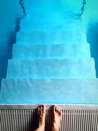 Low section of person standing by steps in swimming pool