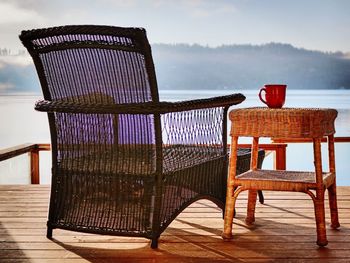 Empty chairs and table at beach against sky