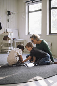 Schoolboys studying with senior female teacher while sitting on classroom floor at preschool