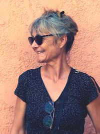 Smiling woman in sunglasses standing against wall