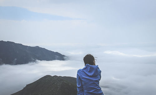 Rear view of woman looking at cloudscape while sitting on mountain