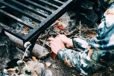 Cropped image of person igniting campfire under metal grate