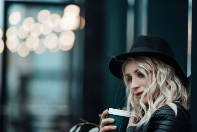 Portrait of young woman holding hat against blurred background