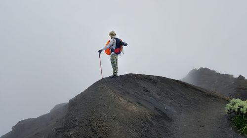 Low angle view of person with backpack standing on mountain against clear sky