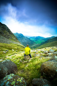 Rear view of man sitting on rock against mountains