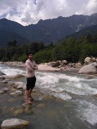 Full length of young man standing on rock against sky