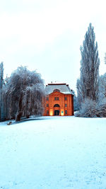 Snow covered house by trees against sky