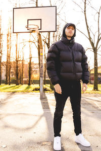 Portrait of young man standing against basketball hoop and trees