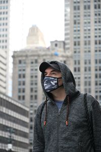 Man wearing mask looking away standing against building