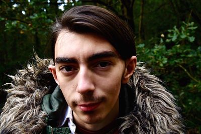 Close-up portrait of young man wearing fur jacket in forest