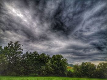 Trees on field against storm clouds