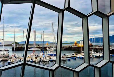 Sailboats moored on sea against sky seen through window