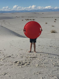 Ten-year-old boy in white sand with red bobsled