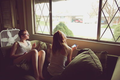 Sisters relaxing on sofa by window at home