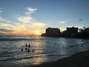 Silhouette people swimming in sea against sunset sky