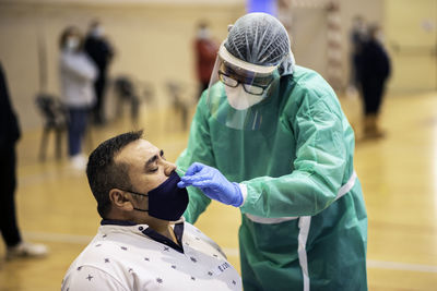 Doctor wearing protective suit checking patient indoors